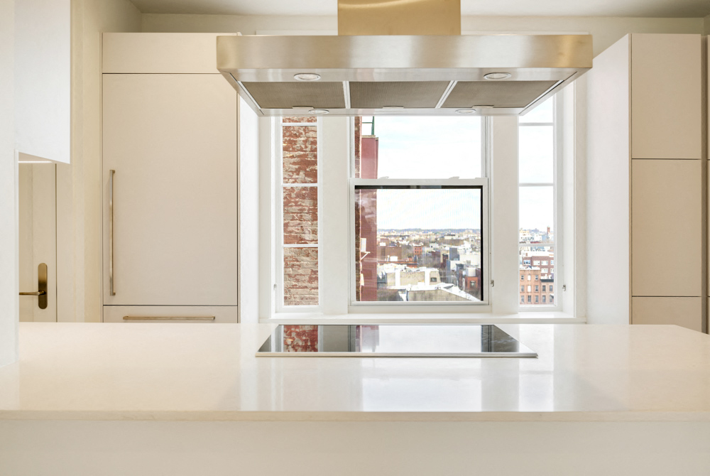 A white kitchen with a large window overlooking a city.